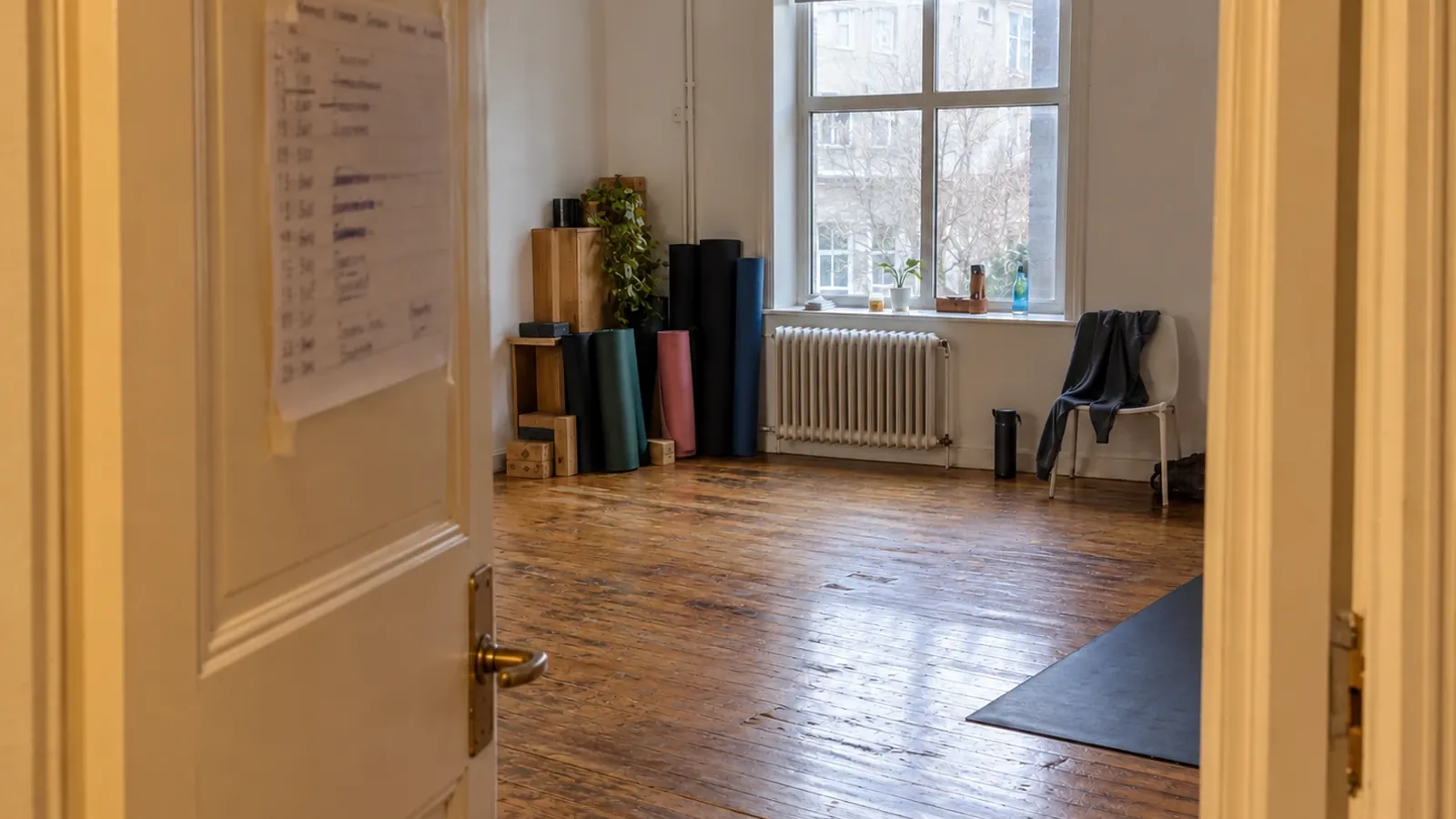 An empty studio room at midday with a handwritten timetable taped to the door